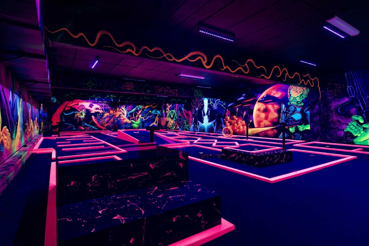 UV-minigolfen hos Panorama Bowling — banene lyser opp i neon-rosa under blacklight, med veggmalerier av astronauter og aliens i bakgrunnen